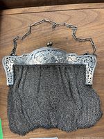 Front view of purse showing draped silver mesh body, decorative top frame with floral cutouts, kiss-lock closure and chain handle.