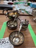 Two open scalloped bowls each holding a condiment spoon, creamer jug, and lidded jar on wood surface