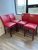 Four red vinyl bar stools grouped together near a window showing overall condition and look.