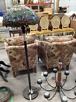 Full view of floor lamp and chandelier base showing floral upholstered chairs and other furniture in background.