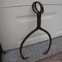 Close-up front view of antique iron block ice carrier resting against a white garage door.