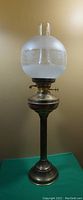 Full view of the tall brass dual wick oil lamp with frosted and etched glass globe and glass chimney on top, showing overall condition and appearance.