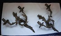 Pair of solid brass wall sconces shown from top view displaying two candle holders and ornate leafy design.