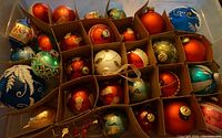 Overhead view of 30 assorted vintage Christmas glass bulbs in various colors and finishes, arranged in individual compartments.