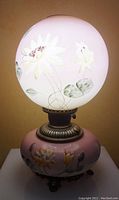 Lighted image of the antique Gone With The Wind style oil lamp with the painted globe and base showing yellow flowers and green leaves.