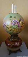 Front view of the antique oil lamp showing floral painted glass globe and brown floral base with metal stand and glass chimney.