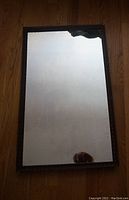 Full front view of antique rectangular mirror showing reflective surface with wavy texture and minor damage.