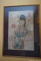 Framed Asian portrait painting hanging on wall, showing entire artwork and frame.
