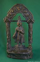 Front view of brass Buddha statue within a decorated temple arch showing detailed facial features, attire, and base.