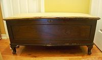 Front view of cedar mahogany blanket chest showing dark exterior, worn top surface without veneer, and cabriole legs.