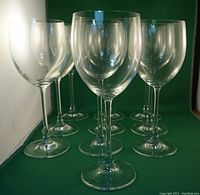 View of six crystal wine glasses with tall stems and rounded bowls on a green background, showing clarity and shape.