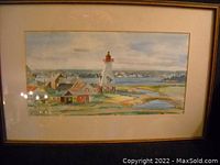 Framed watercolor painting showing a lighthouse and several cottages by a waterfront, signed G Fraser 1979.