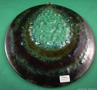 Top view of round handcrafted art glass panel showing mixed green, brown, black, and turquoise colors with bubbles in the glass.