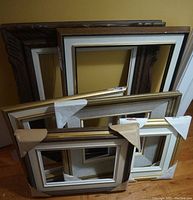 Six assorted art frames stacked showing different frame styles and sizes with protective white corner covers.