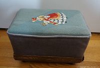 Full side profile of the footstool showing the needlepoint cover, fabric sides, and wood base.