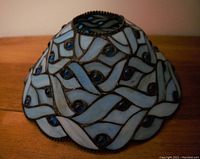 Top and side perspective showing the blue stained glass pieces and blue glass buttons arranged in a wavy pattern with metal beaded trim along scalloped edge.