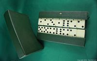 Green leather case, closed and open, displaying bone and ebony dominoes inside. The dominoes have black pips.