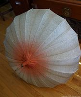 First umbrella photographed opened from above showing orange-red gradient on off-white fabric with wooden shaft and red Lucite handle.