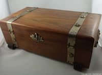 Front angled view of walnut wood box showing tin bands with decorative buttons and metal latch.