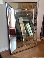 Full view of beveled rectangular glass wall mirror showing reflections and thickness.