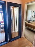 Full view of the large rectangular mirror with padded black pleather frame standing up against the wall.