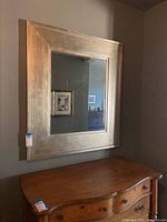 Full view of the large mirror with broad gold painted wooden frame hanging on wall above a wooden cabinet
