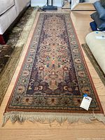 Full view of the vintage runner rug laid out in a living room space, showing floral pattern and fringed ends.