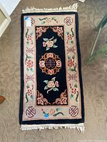 Full view of small rectangular floral throw rug with torn fringe on a carpeted floor.