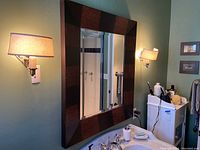 Two beige fabric shade wall sconces mounted on a pale green wall, shown installed on either side of a large mirror. Mirror not included.