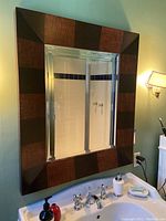 Full view of the large mirror above a sink, showing the reflective glass and wood frame with alternating dark and reddish panels.