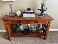 Front view of solid wood side table with decorative elements, two drawers with black metal handles, lower shelf holding decorative items.