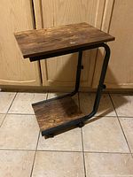 Full view of the adjustable table showing brown wooden top and base with black metal frame.