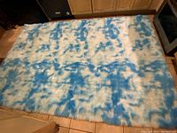 Top-down image showing full rectangular blue and white mottled pattern rug laid flat on tiled floor in kitchen area.