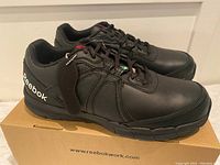Side view of black Reebok steel toe shoes on box showing design and logo.