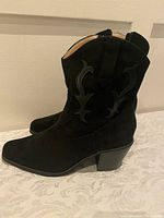 Side view of the black suede boot showing decorative stitching and angled block heel.