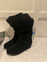 Pair of black wedge boots standing upright with visible mid-calf height and wedge heel.