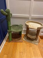 Wide view of green cactus-shaped cat tree with circular green fabric lounge and brown base next to tan two-level carpeted cat tree on wooden floor