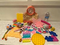 Wide angle photo showing the entire assortment of fidget toys arranged on a table including pop-its, sensory balls, and keychain fidgets.
