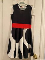 Front view of girls twirly dress featuring black bodice, red waistband, and white skirt with large black circles.