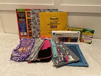 Photo showing various pencil cases with a School Years notebook, Post-it notes pad and a Crayola crayon box
