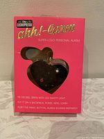 Front view of the unopened pink box displaying the heart-shaped black personal alarm with LED light and panic button