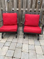 Front view of two matching metal lounge rocking chairs with red cushions placed side by side on stone patio.