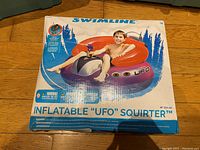 Photo of the boxed Swimline Inflatable UFO Squirter pool float, showing the packaging with a child sitting on the float in a pool.