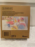Box showing Kidkraft 27-piece cookware playset including colorful pots, utensils, plates, cups for 18 months and older children.