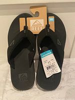 Pair of black Reef men's sandals size 11 with original packaging and tags, showing the front view of sandals.
