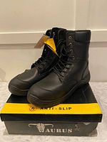 Pair of black workboots displayed on top of Taurus branded shoebox, showing design and ankle height.