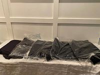 5 pairs of black workpants folded and partially wrapped in plastic on a white surface