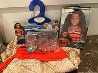 Moana costume dress, wig in package, and necklace on top of costume dress.