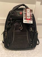 Front view of the new black Swiss Gear backpack showing multiple zippered compartments and brand tags.