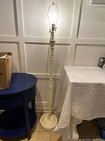 Full view of the white twisted column floor lamp standing on the ground between two tables.